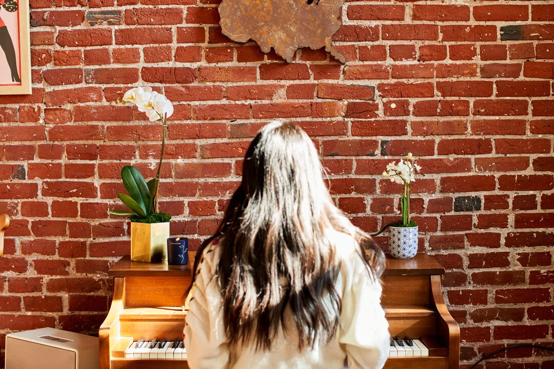 Lifestyle image of woman playing piano while admiring orchids from UrbanStems