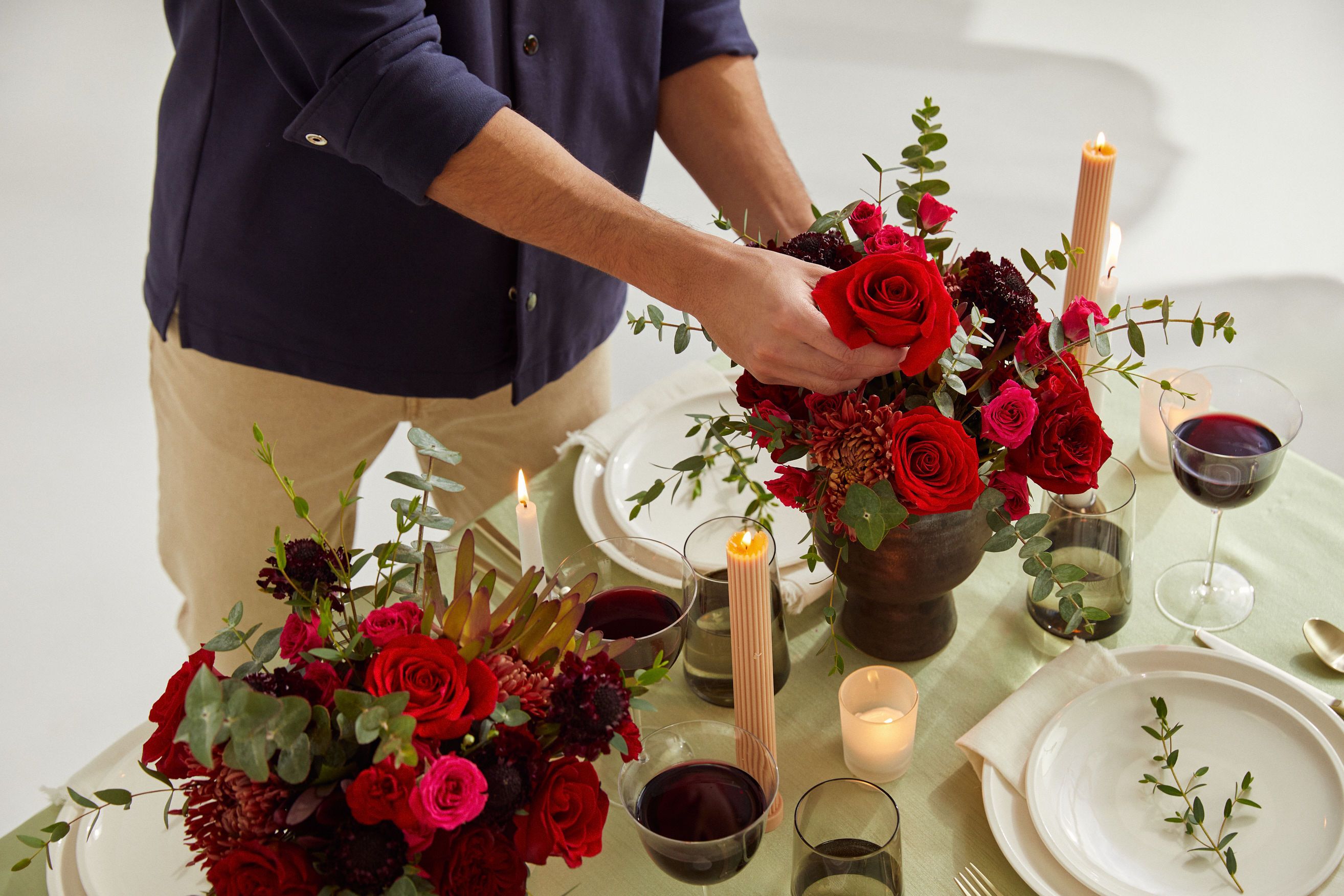 Close up of a man arranging red roses on the dining room table for Valentine's Day.
