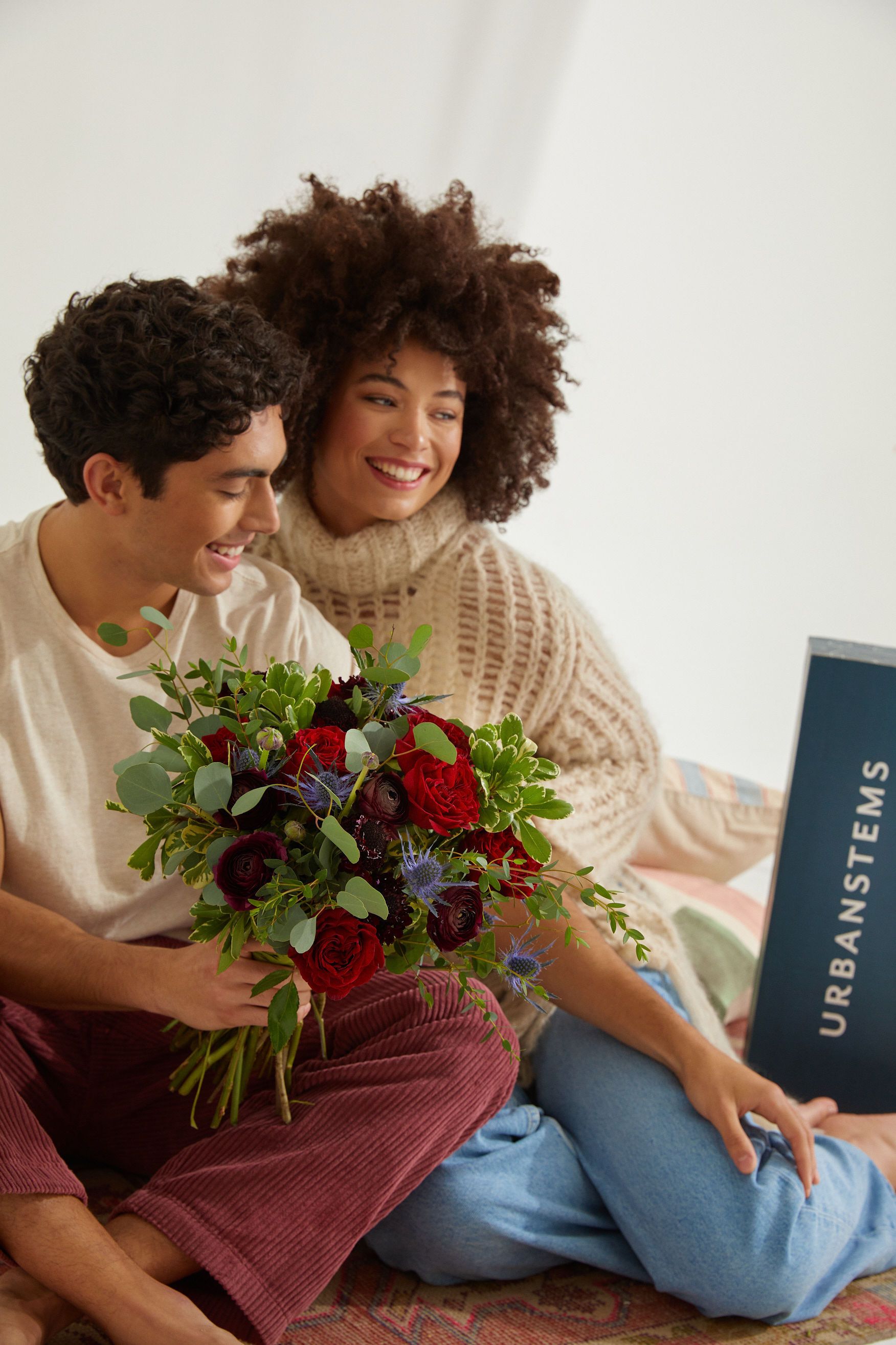 Image of a couple sitting together holding a Valentine's Day bouquet from UrbanStems.