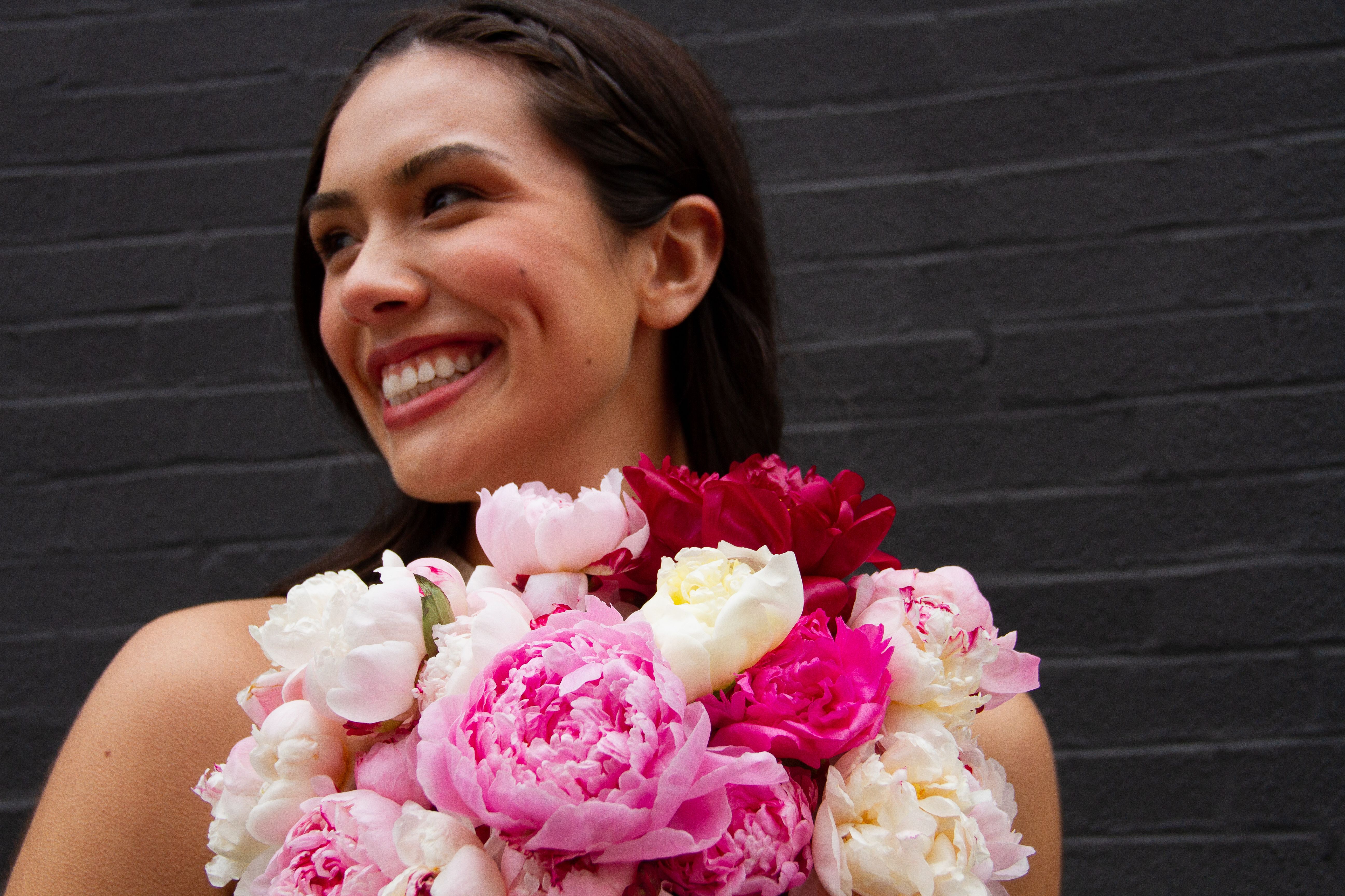 Close up of a woman holding a bouquet of white, red, and pink peonies.