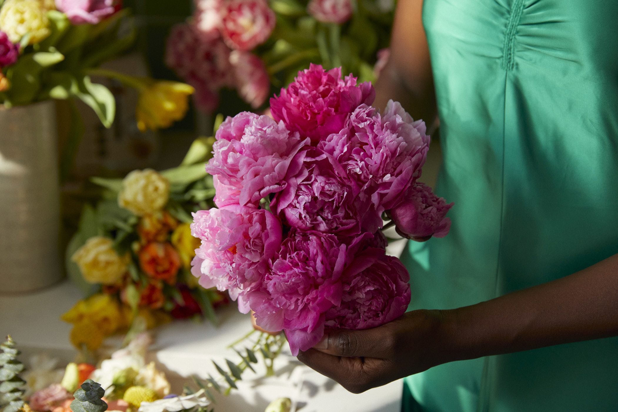 Up close image of pink peonies held by a woman in a green dress.