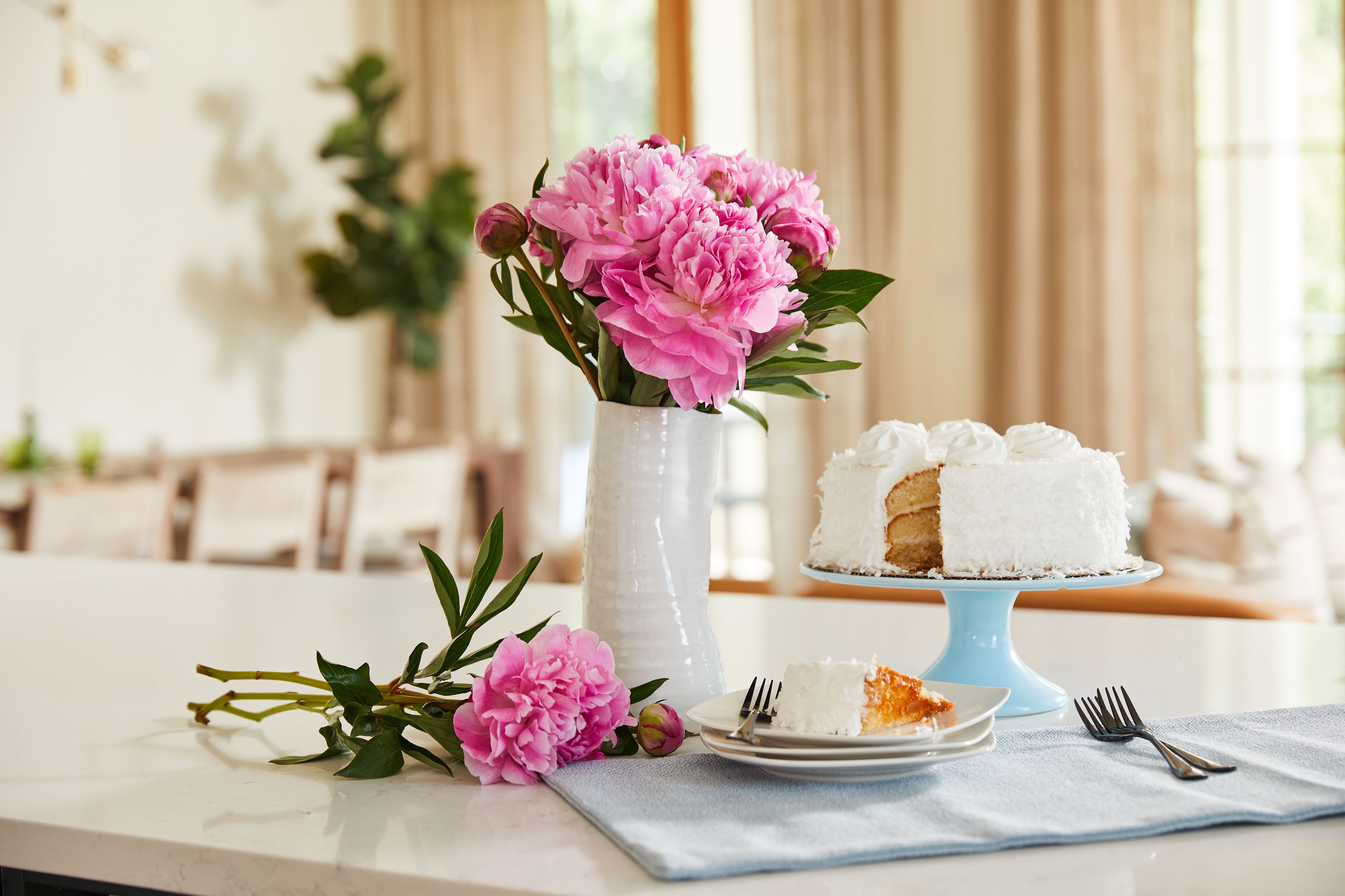 Pink peonies arranged in a white vase on a table with cake