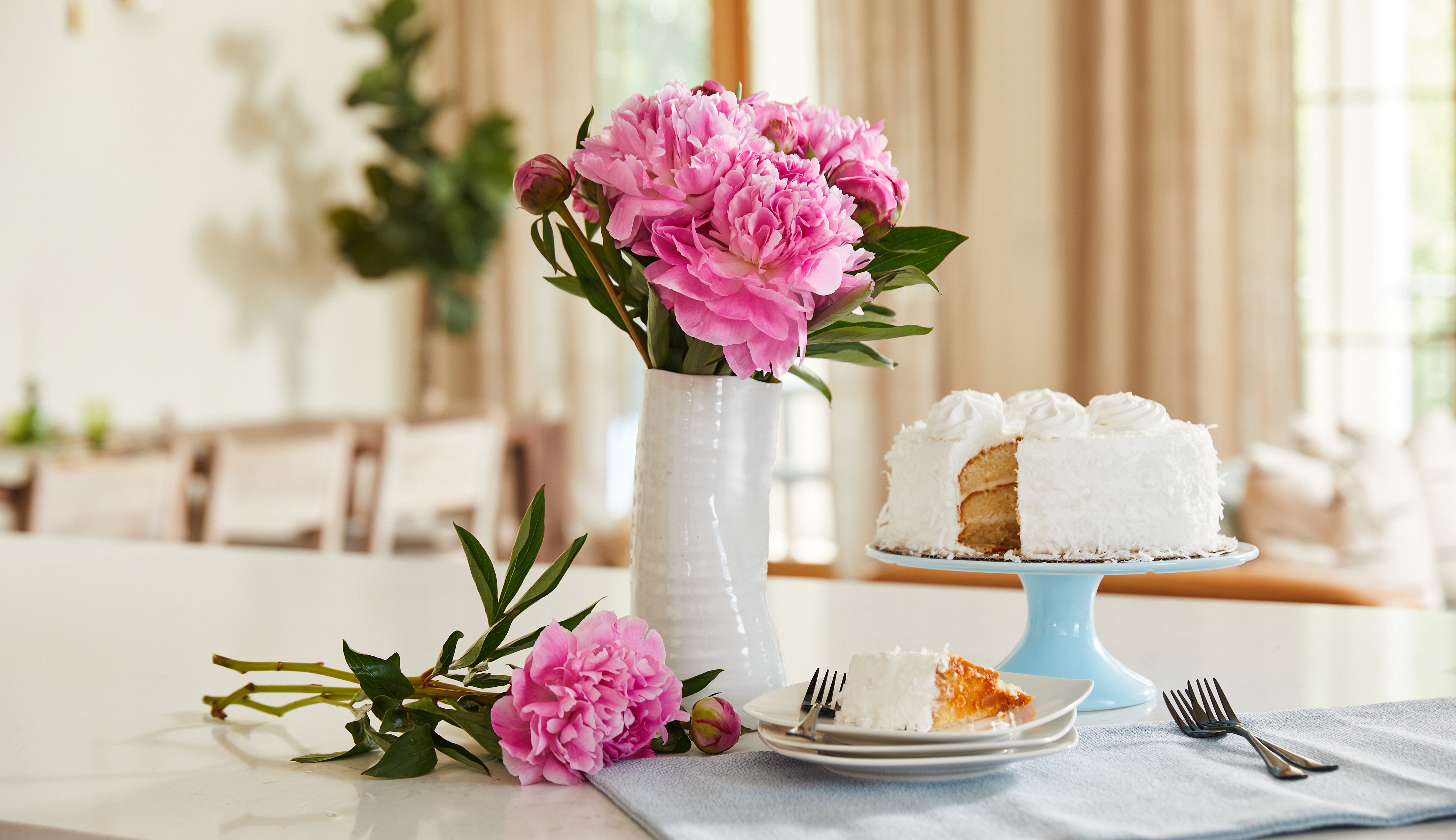 Bouquet of pink peony flowers and white cake on a countertop.