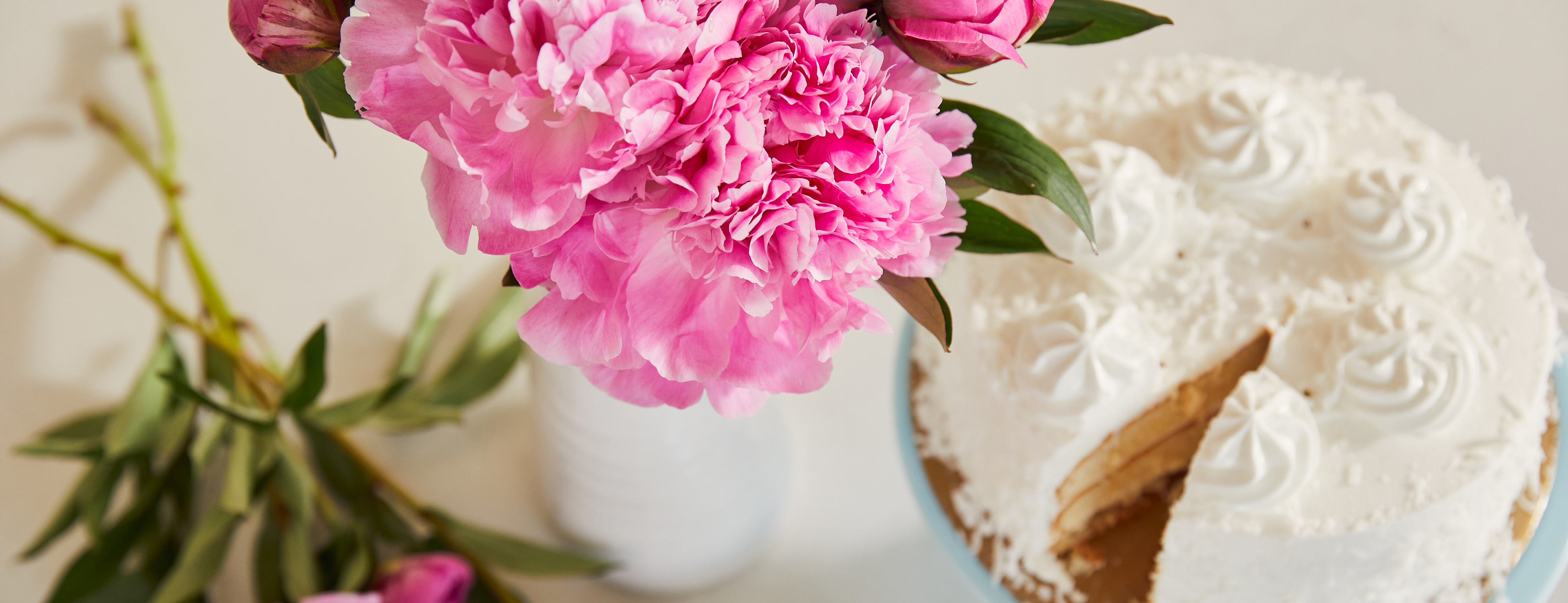 Bouquet of bright pink peonies on a table with frosted white birthday cake.