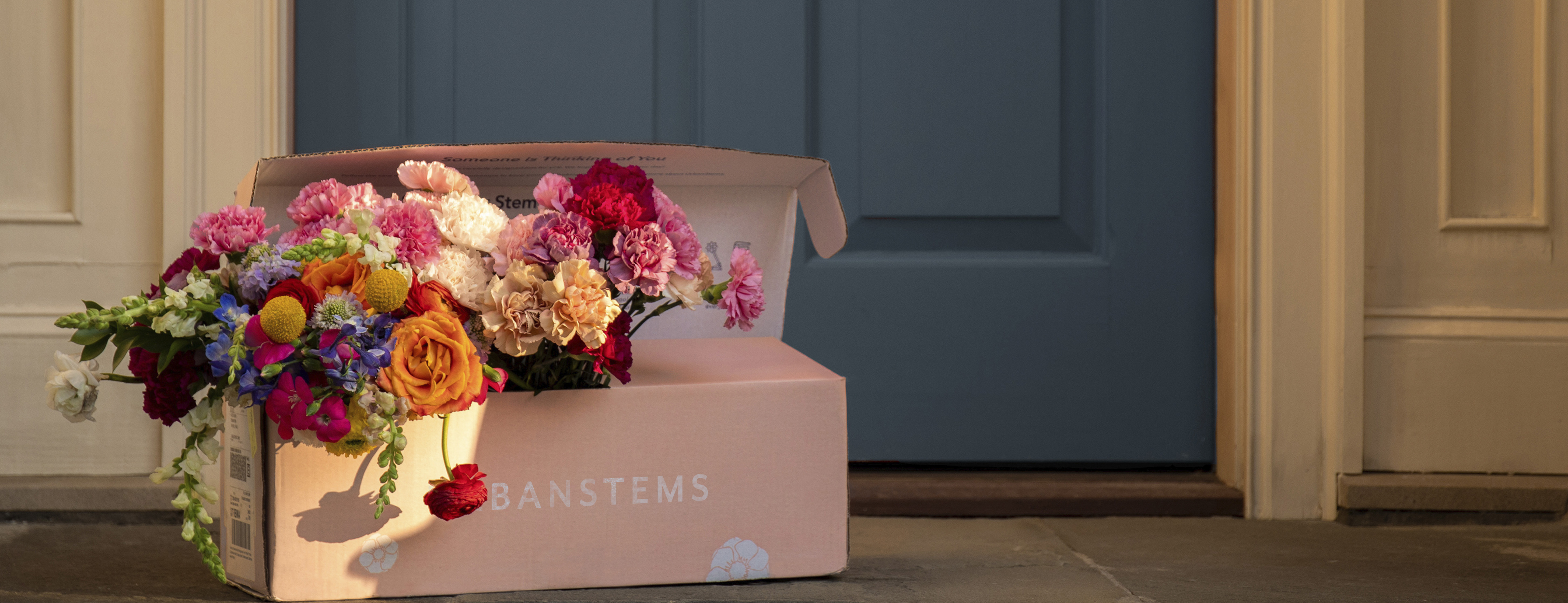 Several floral bouquets in a light pink same-day delivery box on a doorstep