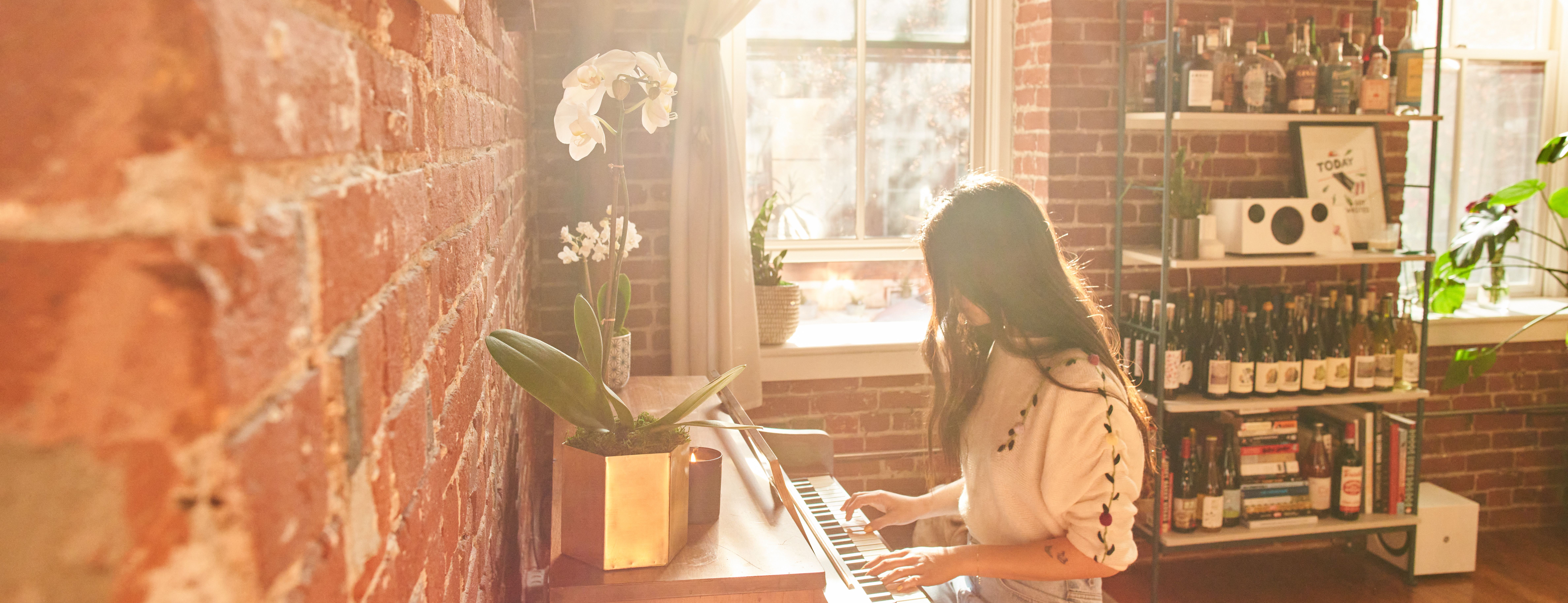 Woman playing piano in the sunlight with two white orchid flowers