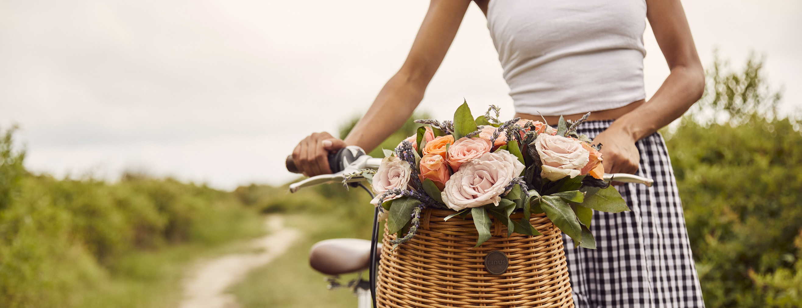 Woman walking a bicycle with a basket full of flowers with a cottagecore aesthetic. 