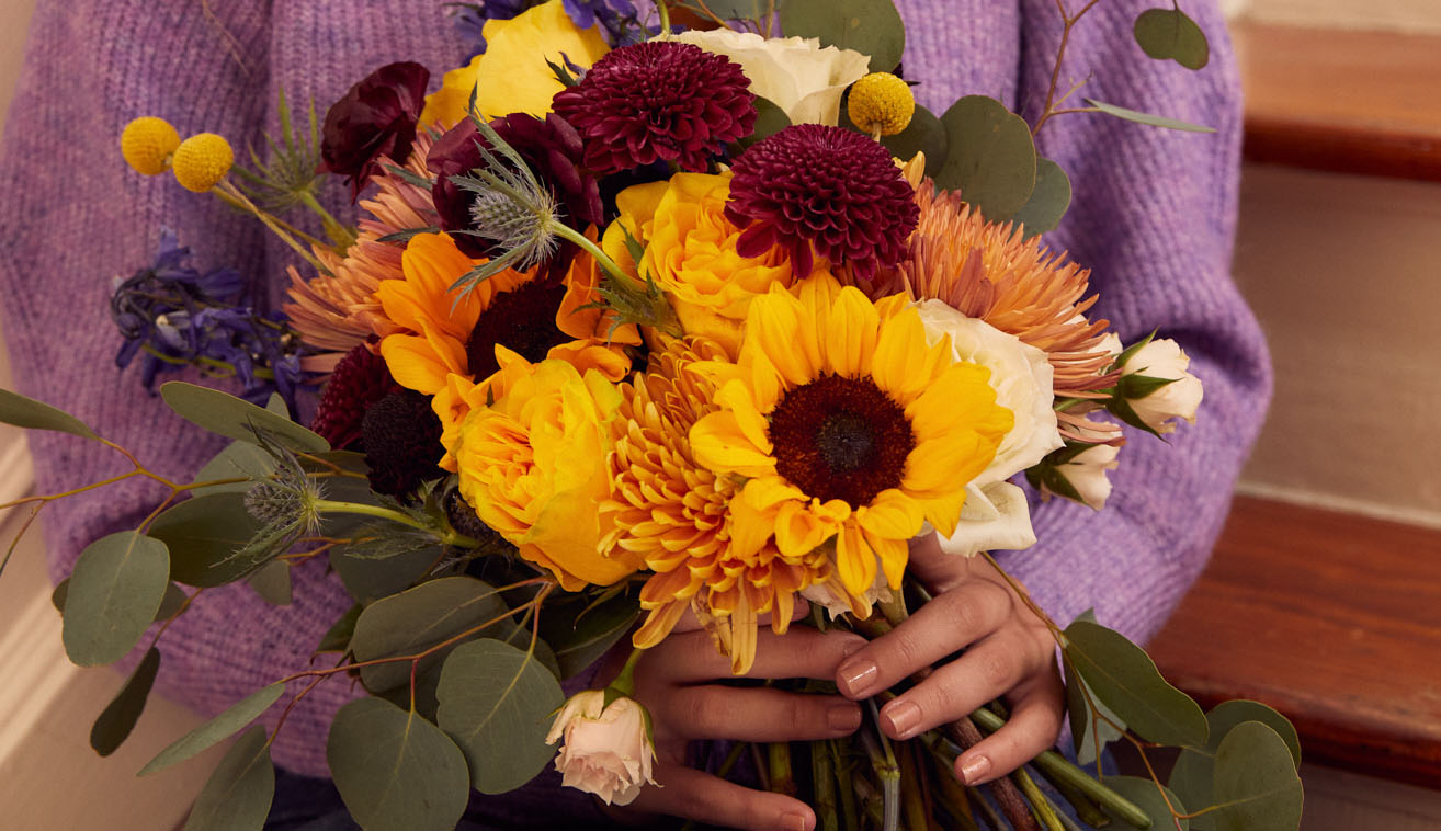 Woman's hands holding bouquets of sunflowers and other fall flowers
