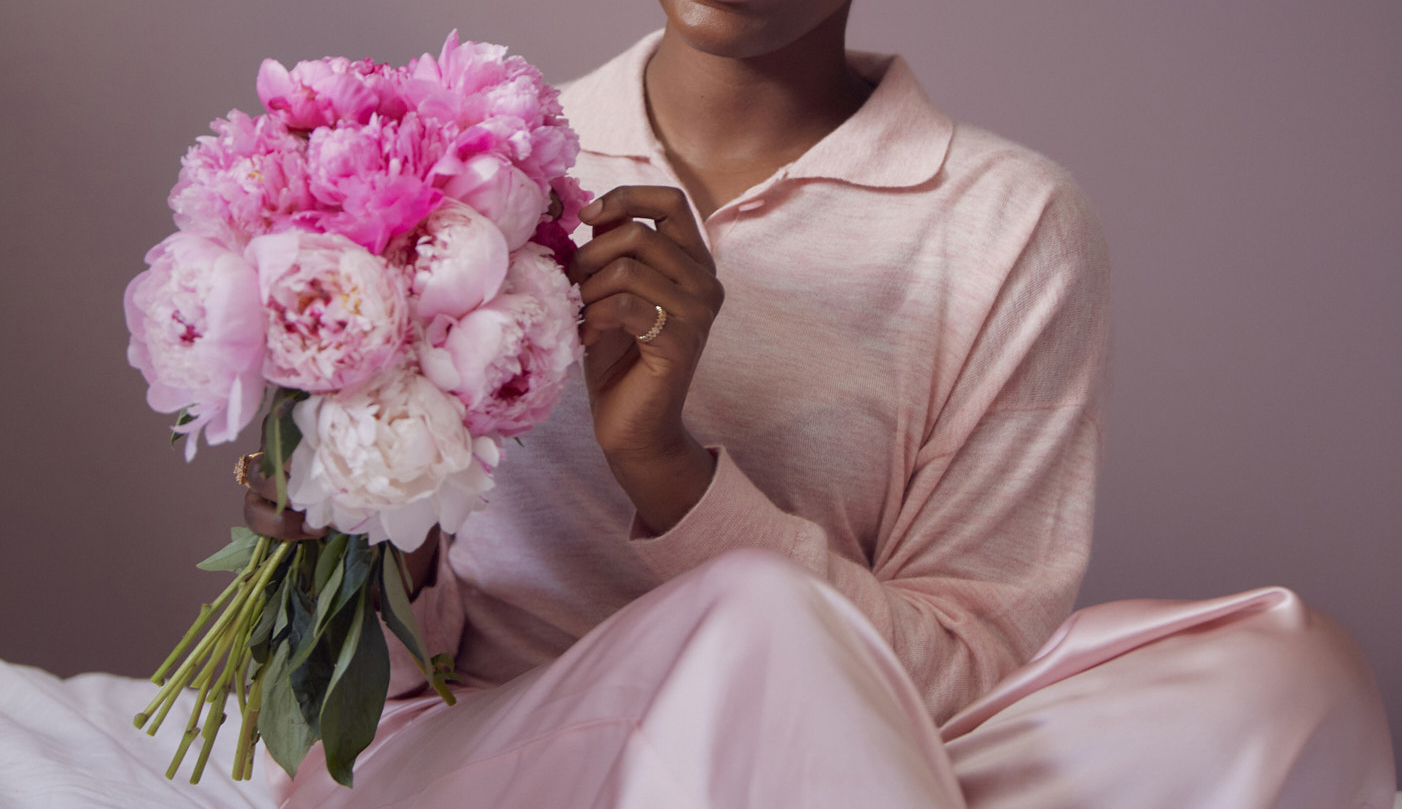Woman sitting on a bed holding a bouquet of pink peonies