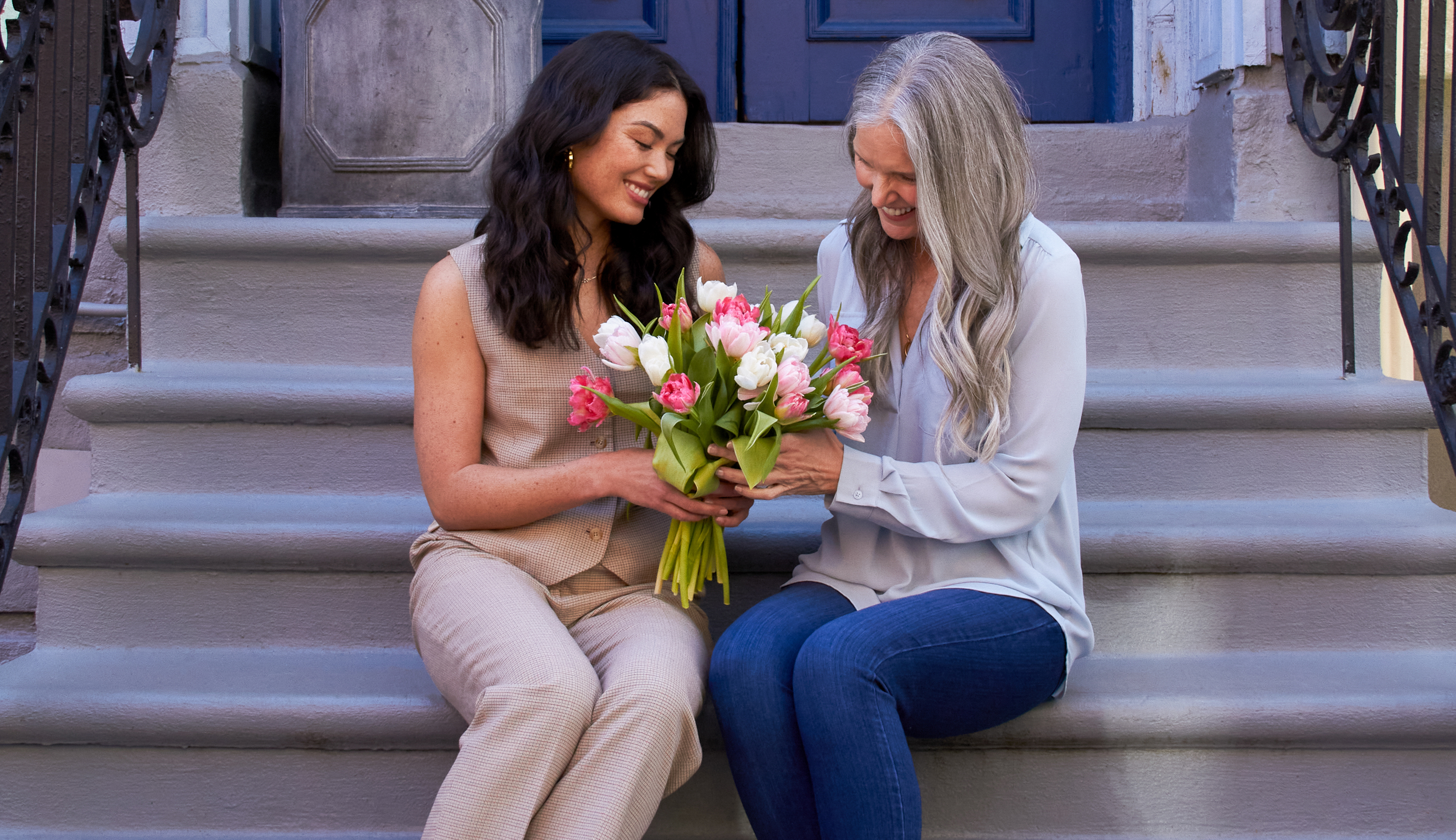Daughter gifting Mother's Day flowers to her mom on the front steps of a building