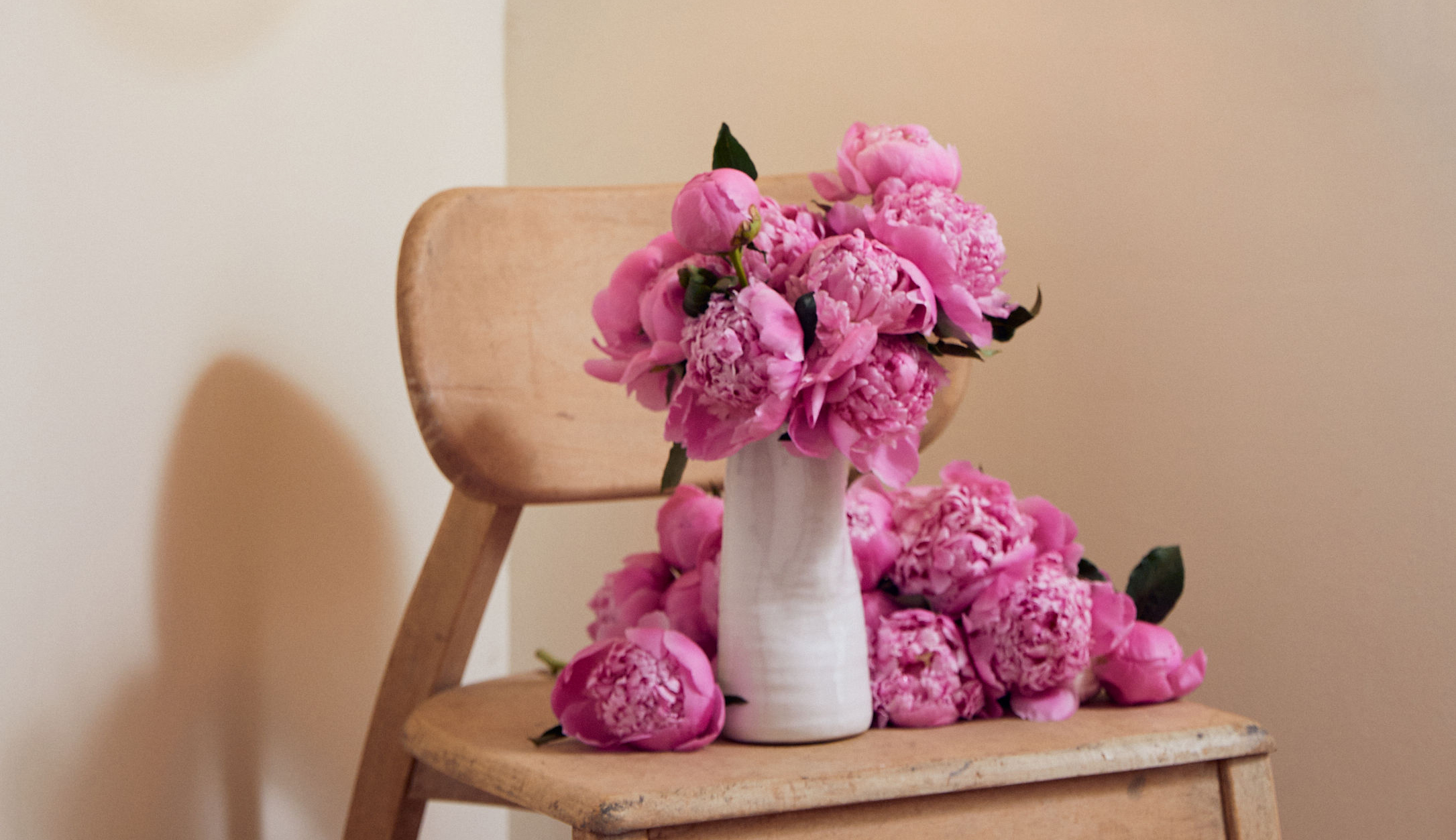 Bright pink peony bouquet resting on a wooden chair