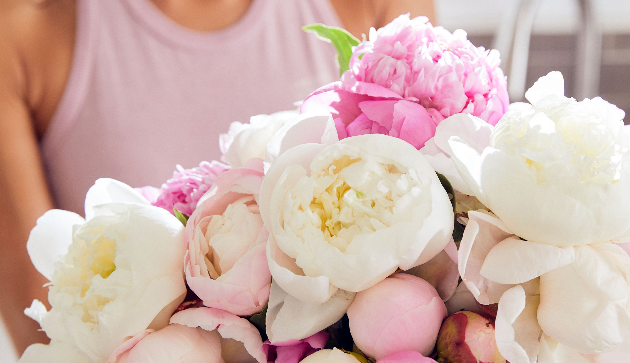 Close up of a woman holding a pink and white peony bouquet